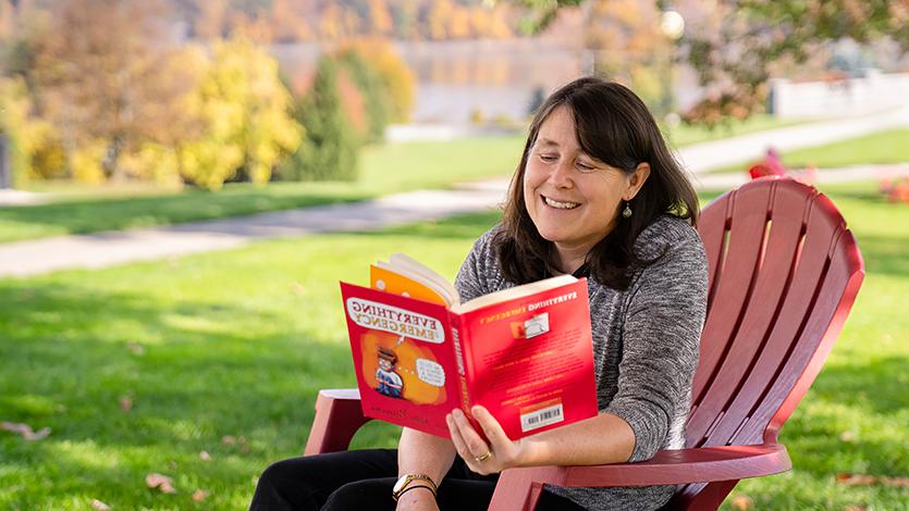 Image of Dr. Fitzgibbons reading a comic book on the campus green.